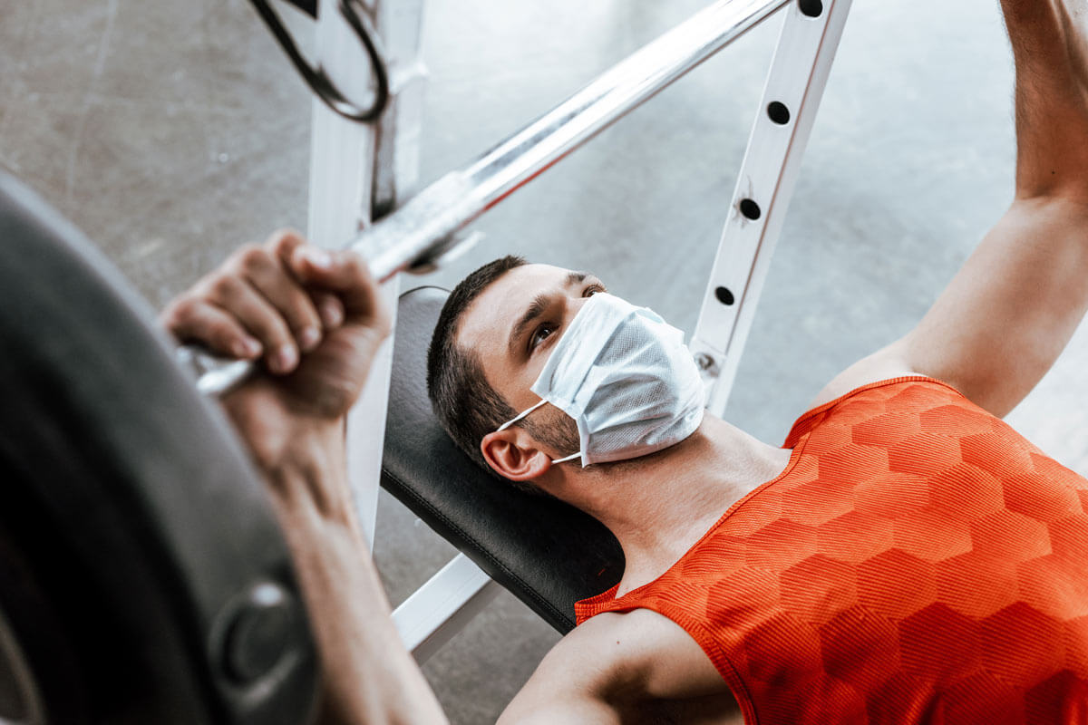 man in mask lifting weights on a bench