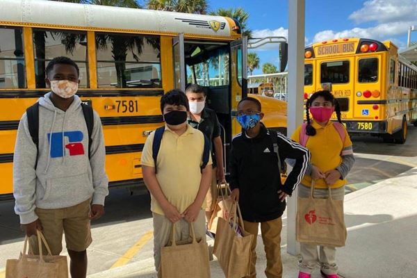 kids holding food bags near school busses