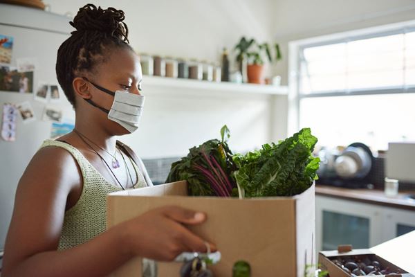 woman in mask holding box of fresh food