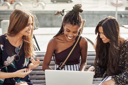 three young women surrounding laptop
