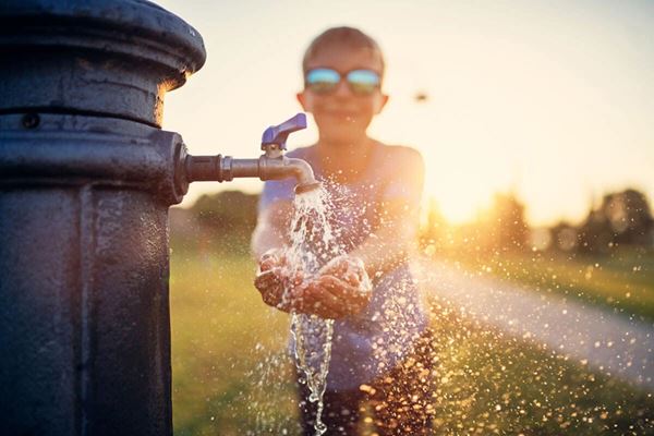 boy cupping water in his hands from park water faucet