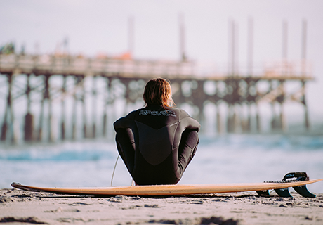 Ventura County contact surfer sitting on surfboard on the beach looking at the pier