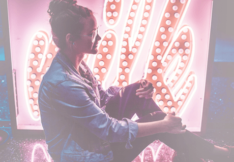 Young woman sitting in front of neon sign