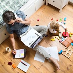 dad on the phone working with toddler next to him playing
