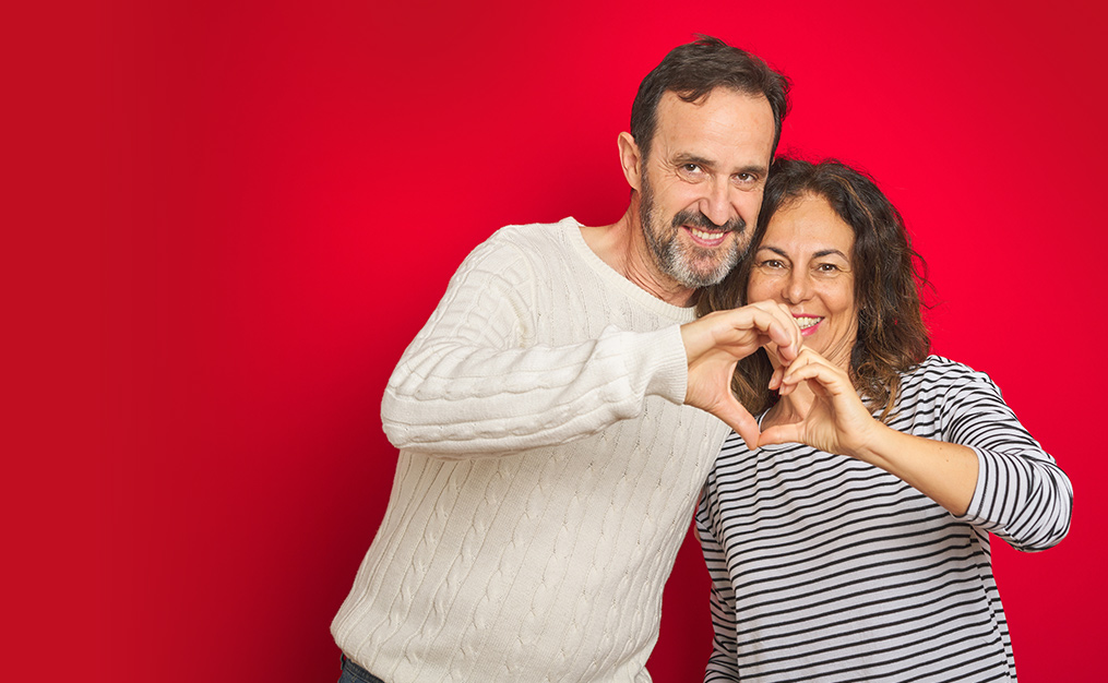 man and woman couple smiling at camera and making heart sign with their hands