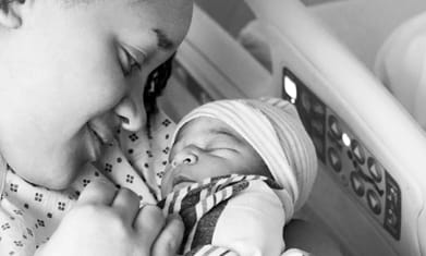 Mixed race young mother smiling down at her newborn child