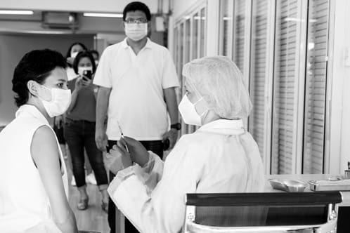 Health worker preparing needle to inject in waiting patient, view of more patients waiting in line for their turn