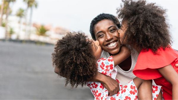 Mother with two daughters, they are kissing her on either cheek while she smiles