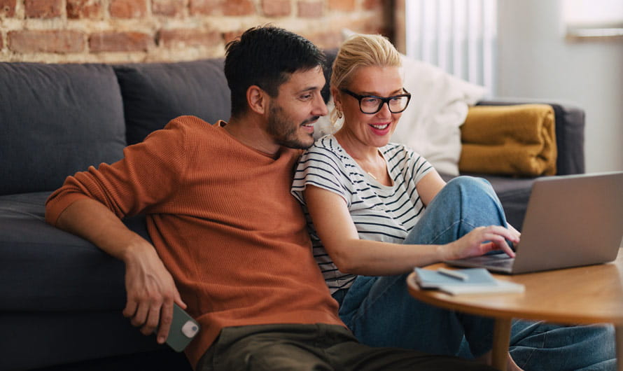 Couple sitting on the floor in front of a sofa working on a laptop together
