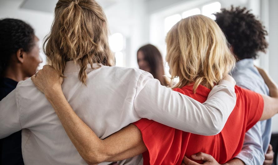 A diverse group of people standing in a circle in a supportive embrace.