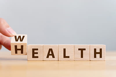 close up of a hand turning a letter block over from an H to a W to change the word Health into the word Wealth