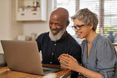 Smiling older couple working together on a laptop in the kitchen