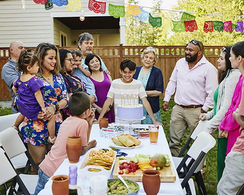 A multigenerational family with a smiling boy waiting to blow out candles on a cake during a backyard birthday party on a summer day