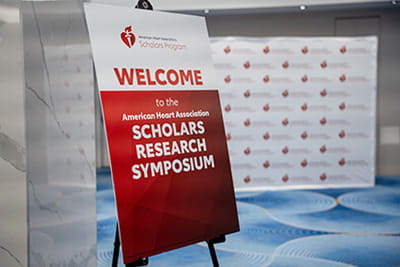 The American Heart Association Scholars Research Symposium welcome sign and step-and-repeat backdrop.