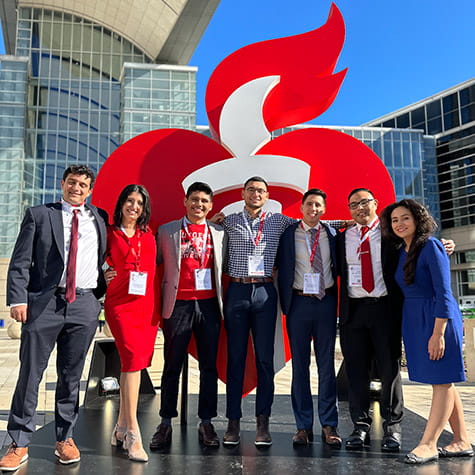 A group of American Heart Association Graduate Program Scholars standing in front of a large heart and torch display
