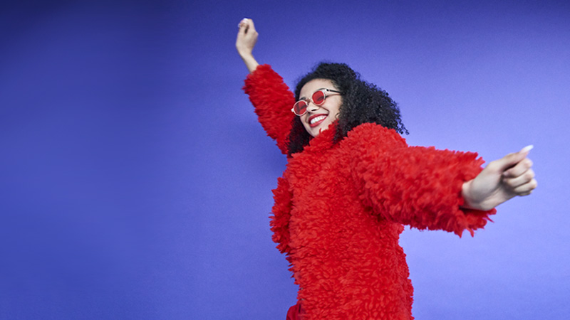 Happy young woman in a furry red coat and trendy glasses dancing on a purple background Happy young woman in a furry red coat and trendy glasses dancing on a purple background