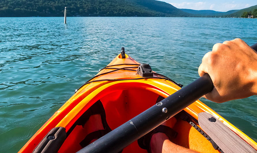 Personal perspective shot of a man paddling an orange kayak on a lake