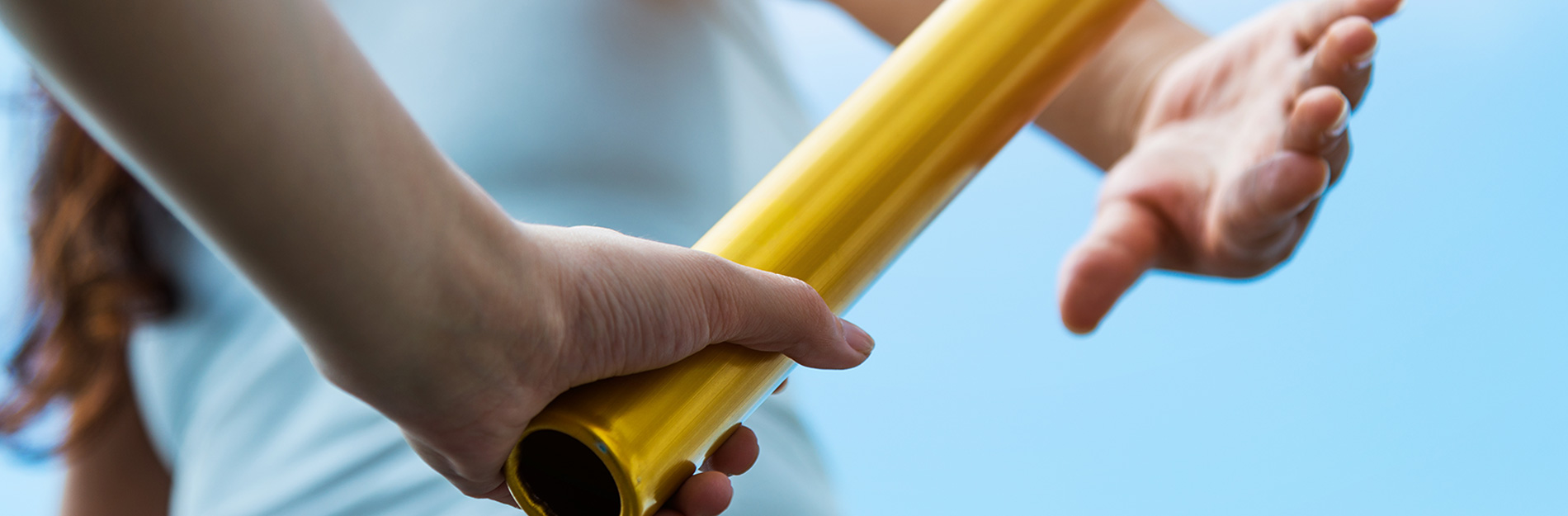 Two hands passing a gold baton during a relay race