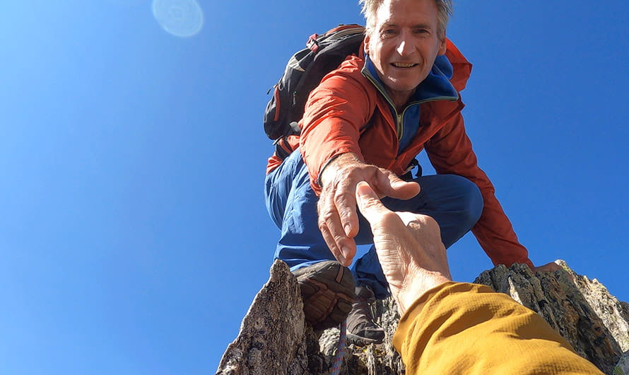 A woman's personal perspective of a rock climber offering a hand up a mountain peak