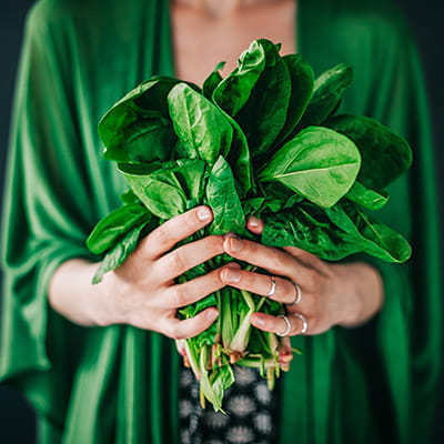 Close-up of a woman in a green dress holding a bunch of spinach leaves