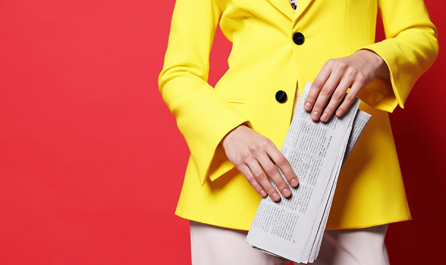 The midsection of a woman in a yellow jacket holding a newspaper against a red background