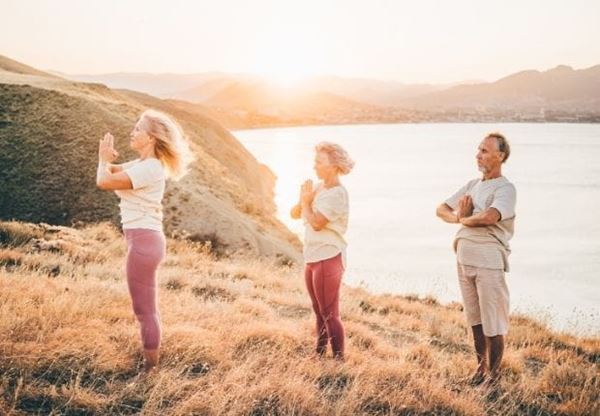 three people meditating on a cliff overlooking a lake