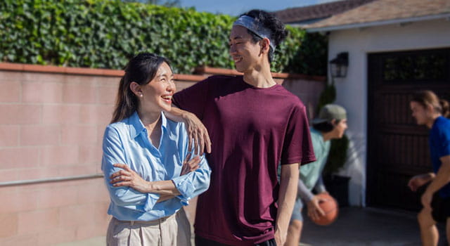 teenage son with mom smiling at each other at backyard basketball court