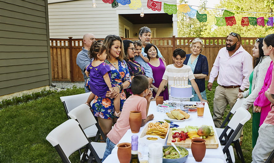 A multigenerational family with a smiling boy waiting to blow out candles on a cake during a backyard birthday party on a summer day.