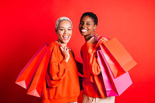 stock image of two women smiling for camera while holding red shopping bags over their shoulders
