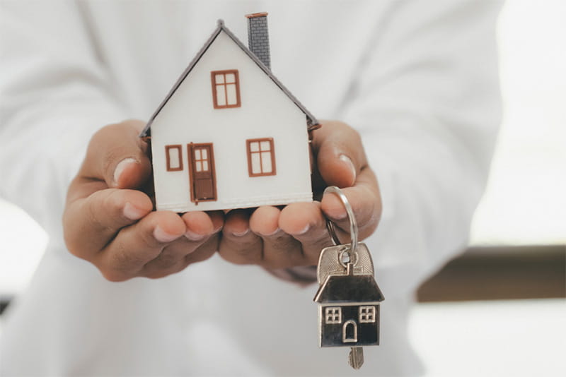 Hands holding out a model house and a keyring with key attached