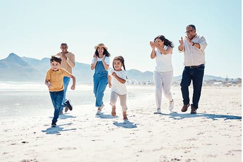 A multi-generational family following their young children as they run happily on the beach