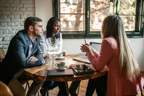 a young couple sitting at a table chatting with an advisor over coffee
