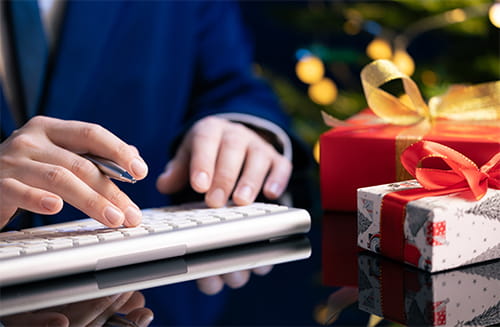 close up view of a man's hands typing on a keyboard next to some wrapped holiday gifts