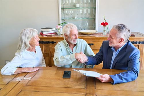 An older couple smiling, shaking hands, and talking with an advisor