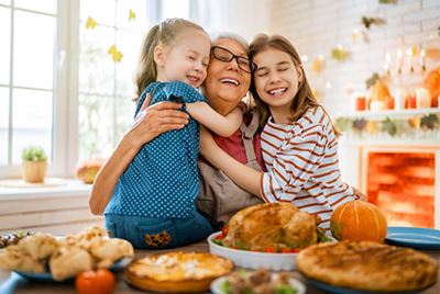 A grandmother hugging her two grandchildren at a holiday table displaying a turkey dinner and other holiday dishes