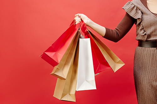 view of a woman's arm holding a handful of paper shopping bags out to one side