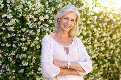 Smiling older woman standing outside in front of flowering bushes