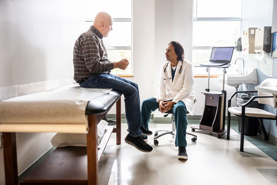 Patient sitting on exam table talking to his doctor