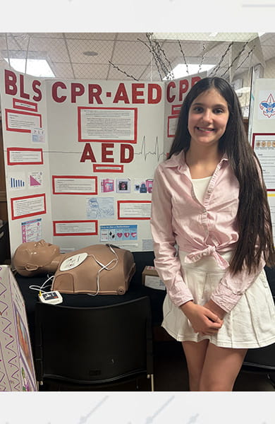 Melina, a sixth-grader, standing in front of the display she made for her school project featuring the importance of CPR and AED education