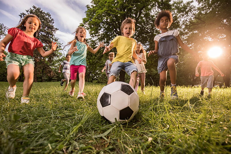 Below view of playful children having fun while playing soccer in nature.