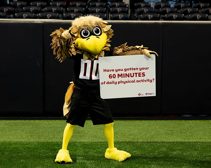 Freddie Falcon, the Atlanta Falcons mascot, standing on the field holding a sign that says "Have you gotten your 60 minutes of daily physical activity?"