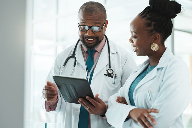 Two doctors smiling and looking at a tablet together