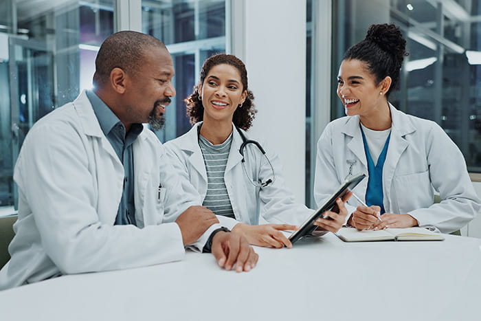 Three health care professionals sitting at a table, smiling while reviewing info on a tablet
