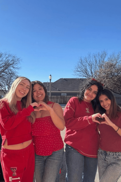 Four students wearing red hold their hands in hearts