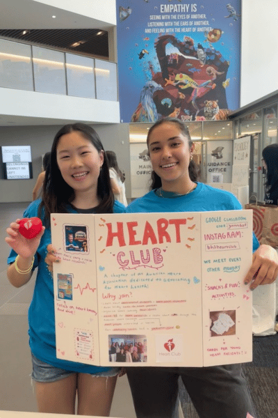 Students holding Heart Club poster at club fair