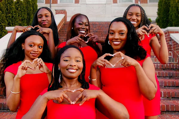 Group of young ladies from a Heart Club wearing red and posing together, making hearts with their hands