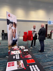 Attendees of Heckerling 2025 stand and talk in front of the AHA info and swag table