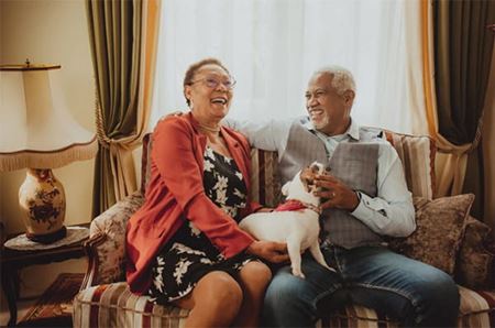Older couple laughing, sitting on the couch with their small dog