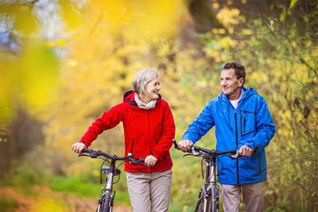 older couple smiling and walking their mountain bikes through fall foliage