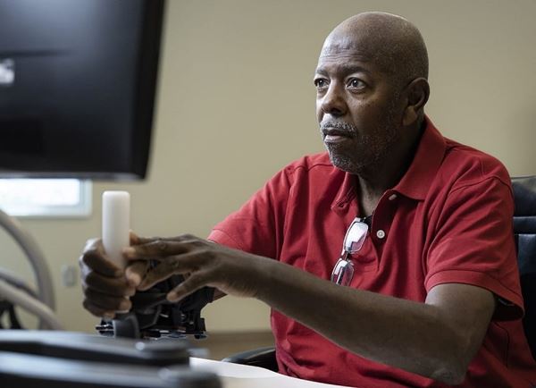 A senior Black man in a red polo is using a controller to interact with a computer. A senior Black man in a red polo is using a controller to interact with a computer.